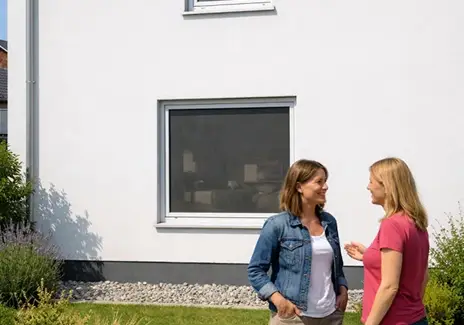 Zwei Frauen stehen vor einem Hausfenster mit eingesetztem Fliegengitter und unterhalten sich