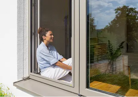 Frau sitzt an einem geöffneten Fenster mit maßgefertigtem Fliegengitter-Spannrahmen SP 1/5