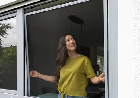 Frau steht an einem geöffneten Fenster mit eingesetztem Fliegengitter-Spannrahmen